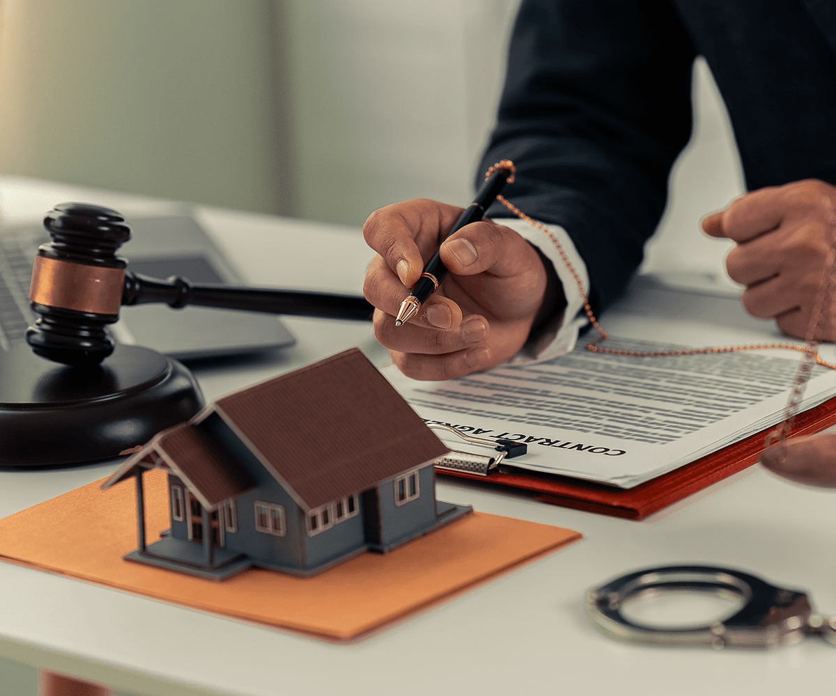 Gavel, contract, model house, and handcuffs on desk.