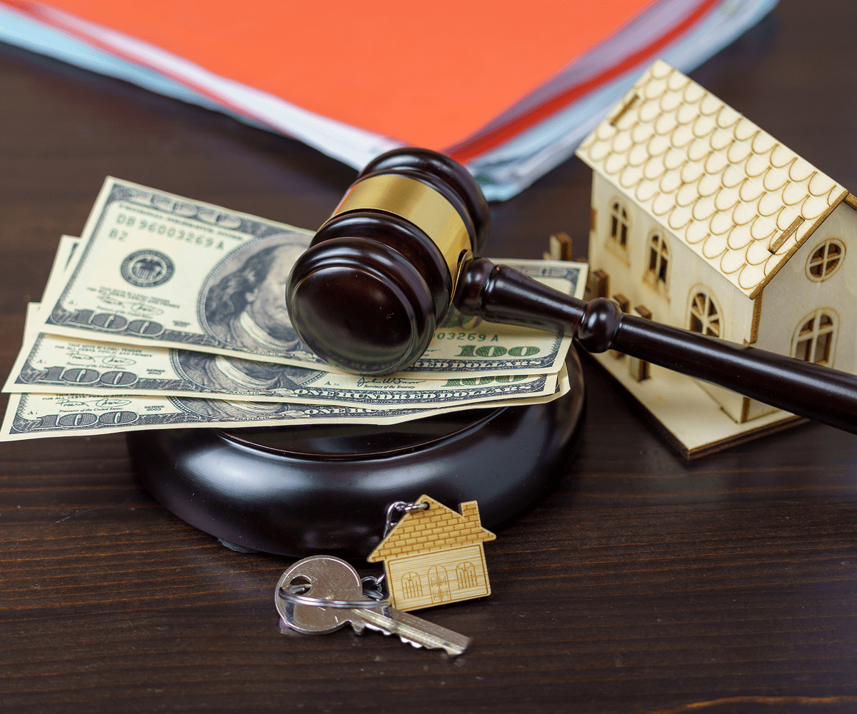Gavel, money, house model, and keys on table.
